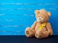 Brown teddy bear sits and a yellow silk ribbon on a blue wooden background, concept of the fight against childhood cancer Royalty Free Stock Photo