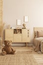 Brown teddy bear sitting on the floor of beige bedroom interior with wooden commode Royalty Free Stock Photo