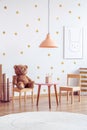 Brown teddy bear on wooden chair next to small table in scandinavian kid`s playroom Royalty Free Stock Photo