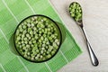 Brown bowl with frozen green peas on napkin, spoon with green peas on wooden table. Top view Royalty Free Stock Photo