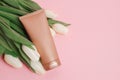 Brown tube with cosmetic cream or lotion for body and bouquet of white tulips, pink background, copy space Royalty Free Stock Photo