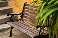 Brown weathered bench with cast iron sides behind a stone staircase in front of a blurred green plant, selective focus Royalty Free Stock Photo