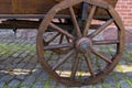 Brown wheel with a wooden rim and spokes at the left rear and the bottom of an vintage cart standing on an old gray stone sidewalk