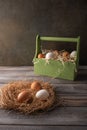 Brown and white chicken eggs in a straw nest on wooden background. Behind a wooden box of eggs in hay. Space under your Royalty Free Stock Photo