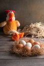 Brown and white chicken eggs in a straw nest on wooden background. Next to a chicken toy. Vertical orientation Royalty Free Stock Photo