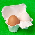 Brown and white fresh eggs inside cardboard paper package on green  fake grass background macro Royalty Free Stock Photo