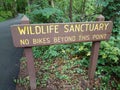 Brown wildlife sanctuary sign with asphalt trail and trees