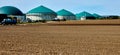 Brown withered field in front of a large plant for energy production from biogas produced in green fermenters by digestion Royalty Free Stock Photo