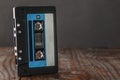On a brown wooden background, there is an audio cassette with a classic black case