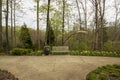 A brown wooden bench on a footpath in the garden surrounded yellow daffodils and purple tulips, lush green trees, grass and plants Royalty Free Stock Photo