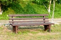 Brown wooden bench in the park. Summer sunny day. Green grass and trees. Resting and relaxing area. Empty bench for sitting. Wood Royalty Free Stock Photo