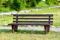 Brown wooden bench in the park. Summer sunny day. Green grass and trees. Resting and relaxing area. Empty bench for sitting. Wood Royalty Free Stock Photo