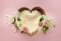 Brown wooden bowl in the shape of a heart for newborn babies on a pink background with a beige shawl, carnations, eustomas