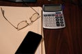 Brown wooden desk with several closed file folders a calculator and glasses turned upside down and a cell phone. Royalty Free Stock Photo