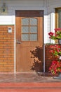 A brown wooden door in a brick wall in the courtyard of a house with a pavement and a bed of flowers. Landscape design