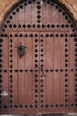 A brown wooden double leaf antique door with metal rivets and a large knocker ring in the oval opening.