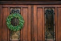 Brown wooden entrance door with green Christmas wreath, drawer for letters mailbox, opaque glass window and wrought iron grill