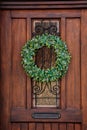 Brown wooden entrance door with green Christmas wreath, drawer for letters mailbox, opaque glass window and wrought iron grill