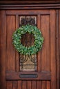 Brown wooden entrance door with green Christmas wreath, drawer for letters mailbox, opaque glass window and wrought iron grill