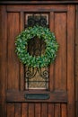 Brown wooden entrance door with green Christmas wreath, drawer for letters mailbox, opaque glass window and wrought iron grill