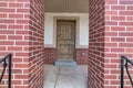 Brown wooden front door of home with red brick porch posts in the foreground Royalty Free Stock Photo