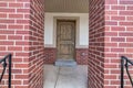 Brown wooden front door of home with red brick porch posts in the foreground