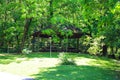 A brown wooden pergola with benches underneath surrounded by lush green trees and grass in the park at Newman Wetlands Center Royalty Free Stock Photo