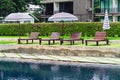 Brown wooden relaxing chairs with big umbrellas beside swimming pool. View of beach chairs placed beside swimming pool in summer Royalty Free Stock Photo