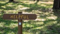 Brown wooden sign in grassy field with helpful written on it