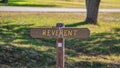 Brown wooden sign in grassy field with reverent written on it