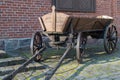 Brown wooden vintage cart, standing drawbar forward on an old gray stone sidewalk against brick wall with shuttered window