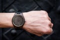 Brown wooden wrist watch with a leather strap on a man& x27;s wrist on a black background. Close-up. Space for your text Royalty Free Stock Photo