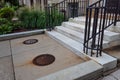 Brownstone entry with marble stairs and iron railings, walkway with manhole covers, beautiful landscaping