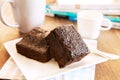 browny cake ready to eat on white dish with coffee cup and magazine book on table top