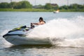 BRP Sea-Doo jet ski watercraft driver in goggles drives water bike at high speed splashing at sunset by river bank. Active summer