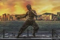 Bruce Lee statue at the Avenue of Stars. Skyline over Victoria Harbour in the background at sunset.