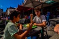 Bruges, Belgium, August 2019. A chip shop overlooking the touristy Markt square. Two Caucasian boys are enjoying the chips with Royalty Free Stock Photo