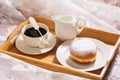 Brunch in bed with freshly roasted and hot bracing coffee, jug of milk, doughnut in powdered sugar on a wooden tray in white Royalty Free Stock Photo