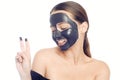 Brunette in black mask for the face. Beautiful girl with perfect skin. A young girl takes care of herself. A girl shows a gesture