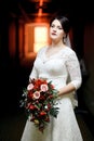 Brunette bride with bouquet standing in hotel hallway, tunnel light.