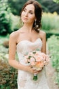 Brunette bride looks away holding peach bouquet in her arms