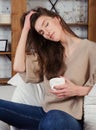 Brunette caucasian girl sits in white armchair with white cup of coffee and touches hair Royalty Free Stock Photo