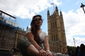 Brunette Caucasian tourist girl resting sitting under the seat of two houses of parliament in Westminster in London