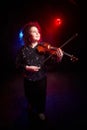 A brunette curly girl in black shiny clothes and with violin on a black background. Model, actress and violinist posing in the