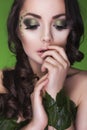 Brunette dryad woman with creative make up and beads on her face, curly hair and costume made of leaves on green backgro Royalty Free Stock Photo