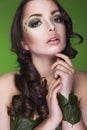 Brunette dryad woman with creative make up and beads on her face, curly hair and costume made of leaves on green backgro Royalty Free Stock Photo