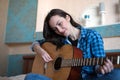 Brunette eastern woman sitting on her bed in the bedroom holding guitar composing a song - musician, songwriter, composer concept Royalty Free Stock Photo