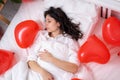 Brunette European girl sleeping on bed with red heart shape balloons.Morning surprise gift on valentines day Royalty Free Stock Photo