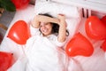 Brunette European girl wake up on bed with red heart shape balloons. Morning love surprise gift on valentines day Royalty Free Stock Photo