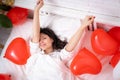 Brunette European girl wake up on bed with red heart shape balloons. Morning love surprise gift on valentines day Royalty Free Stock Photo
